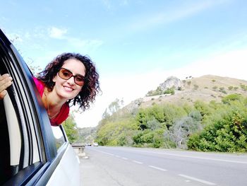 Portrait of smiling young woman on road against sky