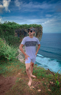 Young man wearing sunglasses standing by sea against sky