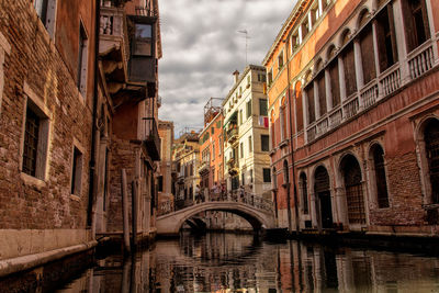 Arch bridge over canal amidst buildings in city