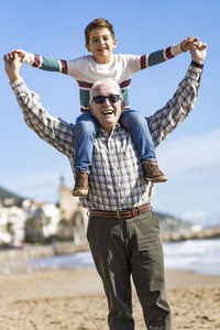 Portrait of happy senior man giving piggyback ride to grandson at beach