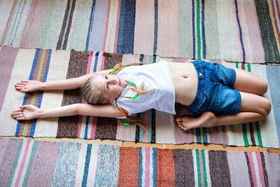 Caucasian girl with braids in a white t-shirt practices yoga, stretches herself on a striped rug