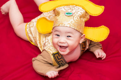 Portrait of cheerful baby wearing costume during chinese new year while lying on red textile