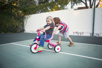 Boy pushing sister sitting on tricycle at yard