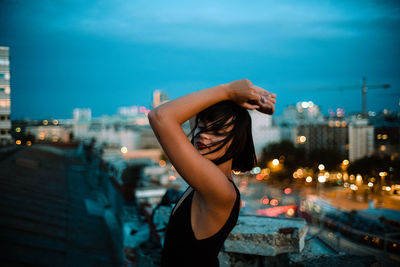 Side view of woman in city against sky at night