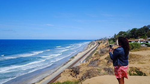 Woman using mobile phone while standing on sand at beach