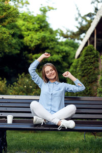 Young woman sitting on bench against plants