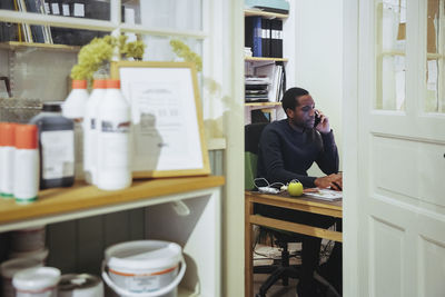 Confident young male store owner talking on smart phone while sitting at desk