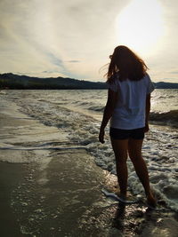 Rear view of woman standing on beach during sunset