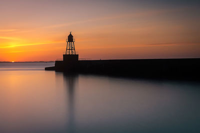 Lighthouse by sea against sky during sunset