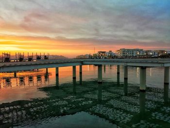 Scenic view of river by buildings against sky at sunset