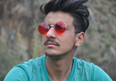 Portrait of young man sitting outside with wearing sunglasses and looking sideways 