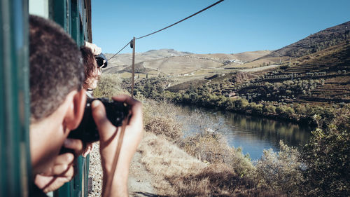 Midsection of man photographing water on landscape against sky