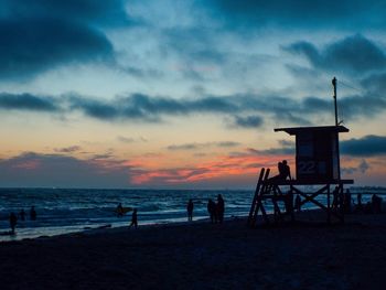 Silhouette people standing on beach against sky during sunset