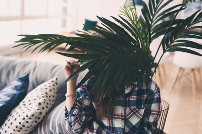 Girl covering face with plants at home