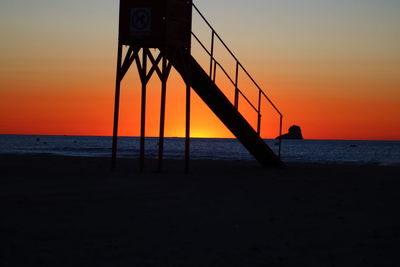 Silhouette lifeguard hut on beach against sky during sunset