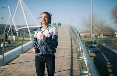 Young woman jogging on footbridge against sky