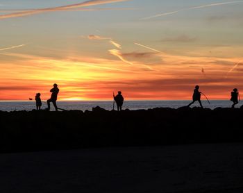 Silhouette people on beach against sky during sunset