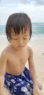 Midsection of shirtless boy at beach against sky
