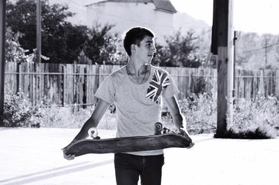 Young man holding skateboard looking away while standing on footpath