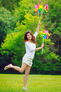 Portrait of beautiful smiling woman holding pinwheel toys while standing on field