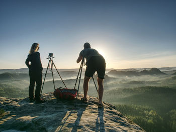 Creative artists stay at cameras on tripods. hikers and photo enthusiasts work together on cliff