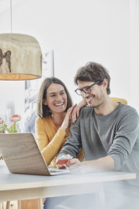 Happy couple with a card using laptop on table at home