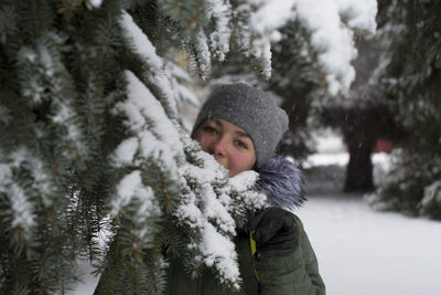 Portrait of girl standing by pine tree during winter