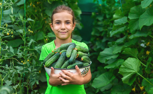 Portrait of smiling girl holding cucumbers at farm