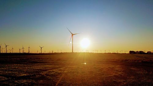Wind turbines on field against clear sky during sunset
