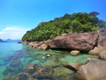 Scenic view of rocks by sea against sky