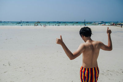 Rear view of boy standing on beach against clear sky