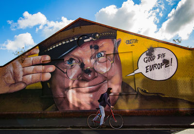 Graffiti on bicycle by wall against sky in city