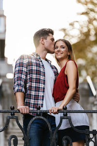 Low angle view of man kissing woman forehead while standing outdoors