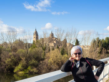 Portrait of smiling senior woman standing on footbridge over river during sunny day