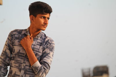 Portrait of young man looking away while standing against wall