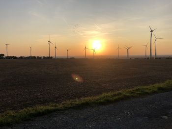 Wind turbines on field against sky during sunset