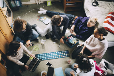 High angle view of teenage girls and boys playing board game in bedroom