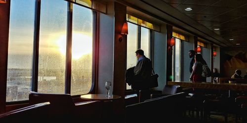 Man standing by window at sunset