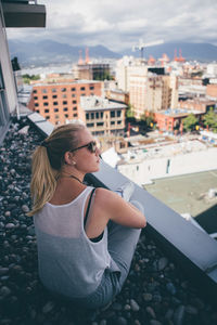 High angle view of woman wearing sunglasses while sitting on building terrace