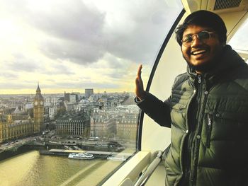 Portrait of smiling man standing in millennium wheel by thames river in city