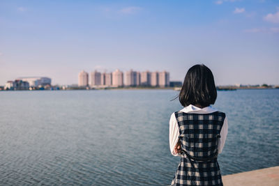 Rear view of man looking at sea by cityscape against sky