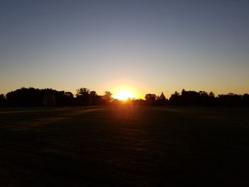 Silhouette trees on field against clear sky during sunset