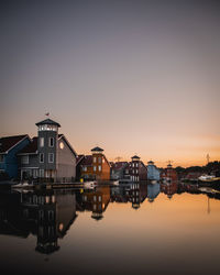 Reflection of buildings in lake against sky at sunset