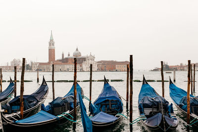 Gondolas moored by wooden posts in canal with church of san giorgio maggiore in background
