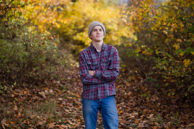Confident teen boy stands in woods alone with arms crossed.