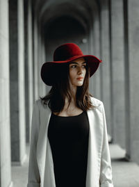 Young woman wearing hat while looking away standing in corridor