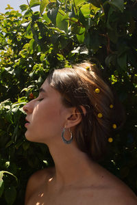 Close-up of shirtless woman with eyes closed standing by plants