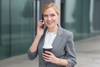 Businesswoman holding coffee while talking on smart phone