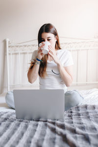 Young woman using mobile phone while sitting on bed at home