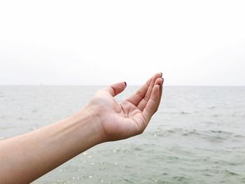 Cropped hand of woman over sea against clear sky